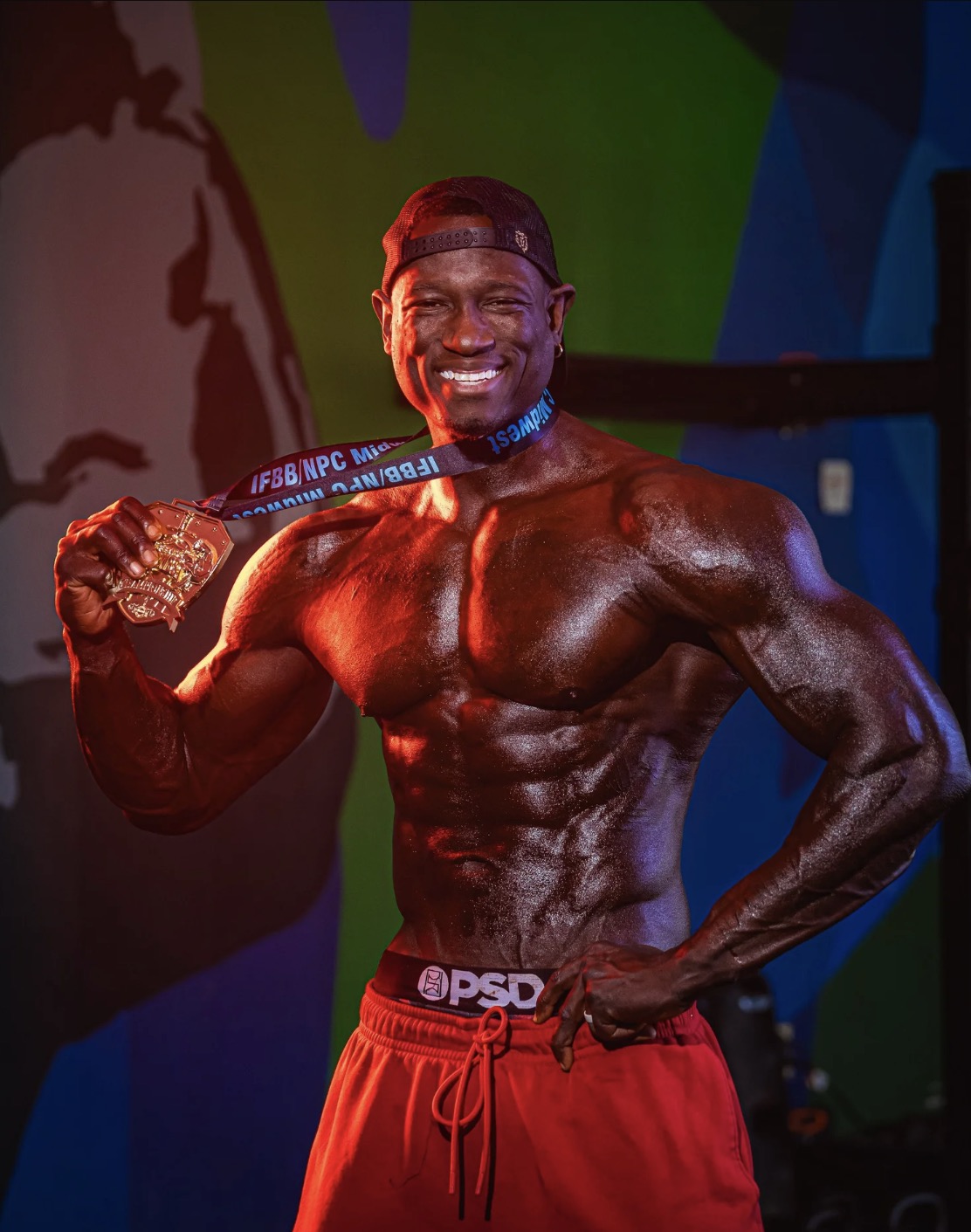 Lawrence Gordon smiling and holding up an IFBB NPC Midwest medal