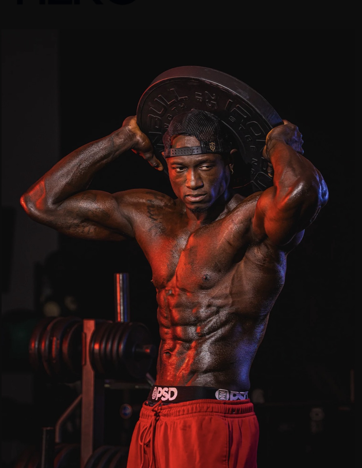 Coach JR pressing a weight plate overhead in a dark gym