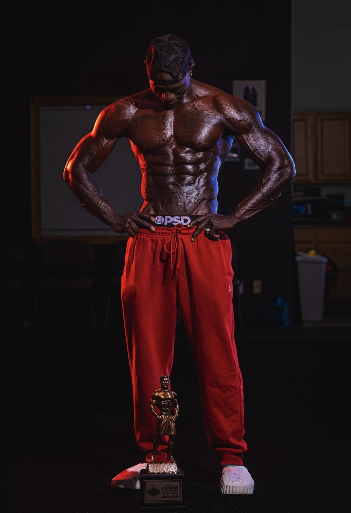 Lawrence Gordon looking down at the 2026 NPC Missouri State overall winner trophy at his feet