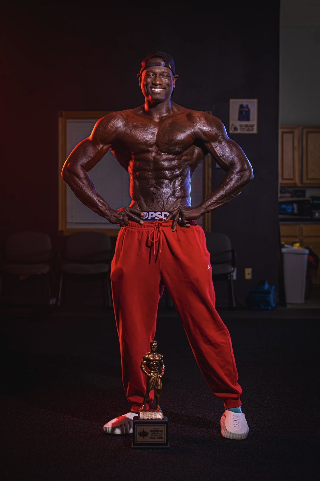 Lawrence Gordon smiling with hands on hips, the 2026 NPC Missouri State overall trophy at his feet